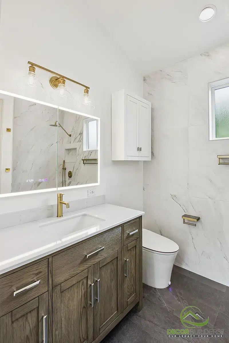 Bathroom remodel featuring a dark wood vanity, white marble countertop, gold fixtures, backlit mirror, and marble tile walls in Morgan Hill, CA