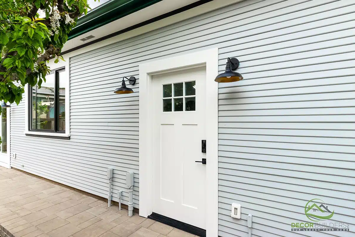 Custom ADU construction featuring a white exterior with barn-style garage door, wall sconce lighting, and concrete pathway in Morgan Hill, CA