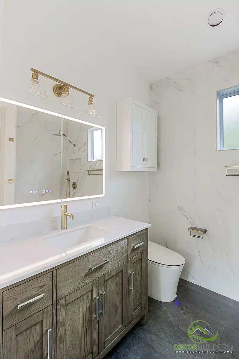 Bathroom remodel showcasing a dark wood double vanity, white marble countertop, backlit mirror, gold fixtures, and white walls in Morgan Hill, CA