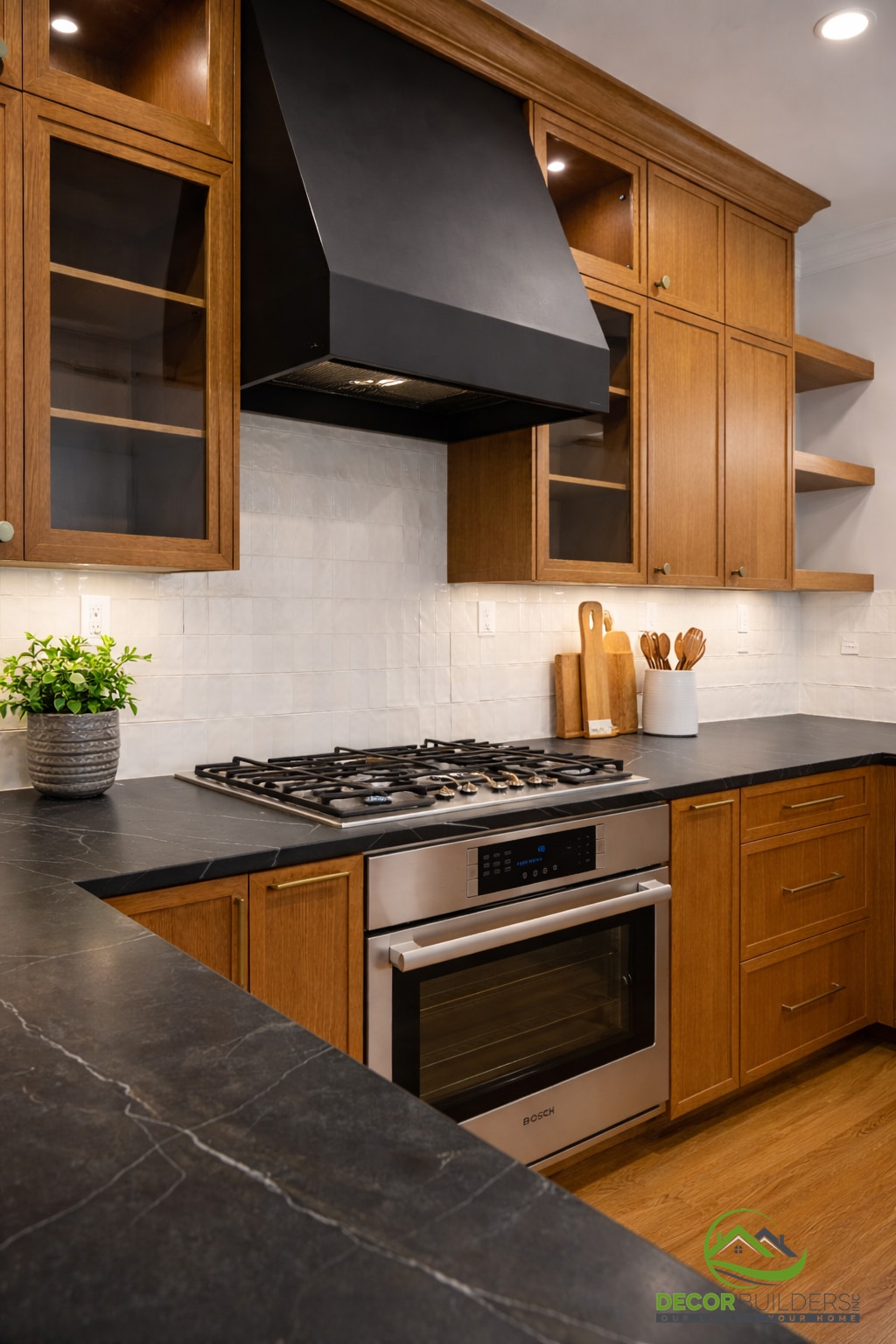 Kitchen renovation featuring a gas cooktop, dark soapstone countertop, stainless steel appliances, and a black range hood with wood cabinetry in Palo Alto
