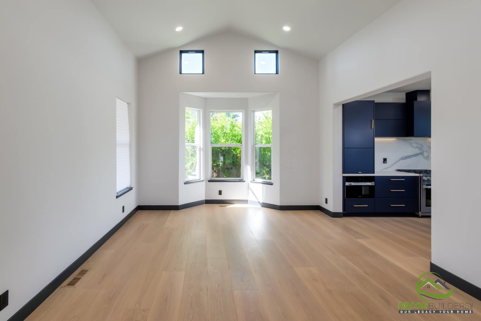 Living room with vaulted ceiling, bay window, and hardwood floors opening into the kitchen, an example of building a custom home in Campbell, CA